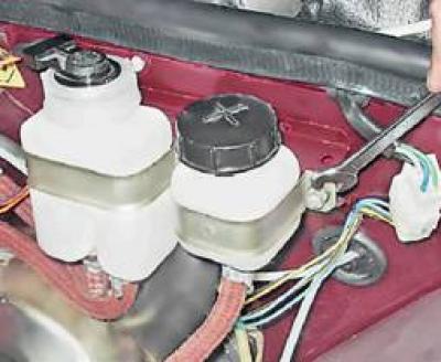 3. Ключом на 10 мм отворачиваем гайку хомута крепления бачка к перегородке моторного отсека.